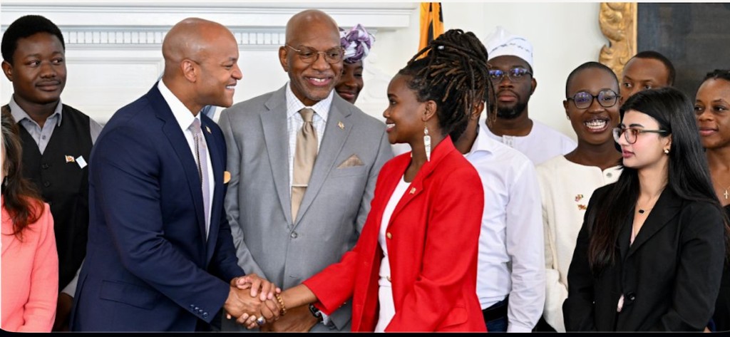 Victoria Merab Akinyi in a red blazer at a formal handshake with colleagues